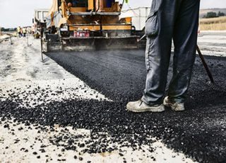Asphalt Road Construction - Picture of a worker operating an asphalt paver machine during road construction.